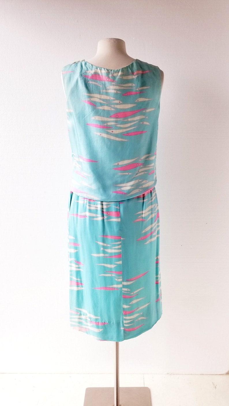 May include: A sleeveless dress with a blue background and a pink and white fish pattern. The dress is on a white mannequin.