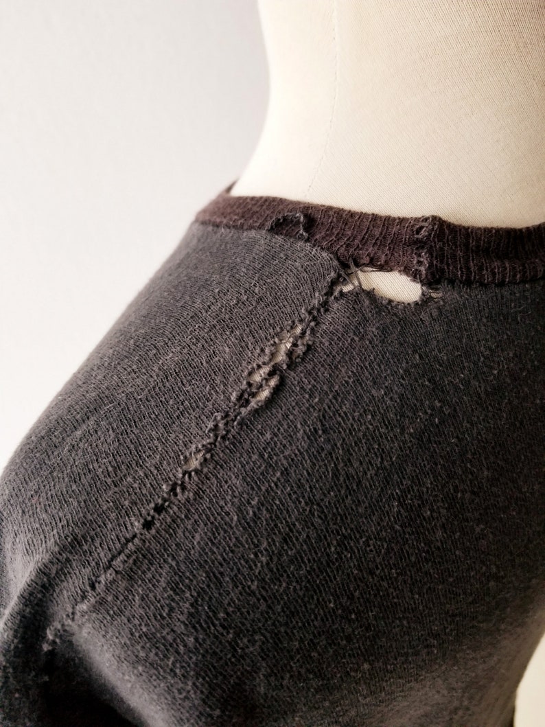 K&ouml;nnte beinhalten: Ein dunkelgraues T-Shirt mit einem kleinen Riss im Nackenbereich.