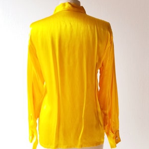 Puede incluir: Una blusa de sat&eacute;n amarillo brillante con mangas largas y cuello abotonado.