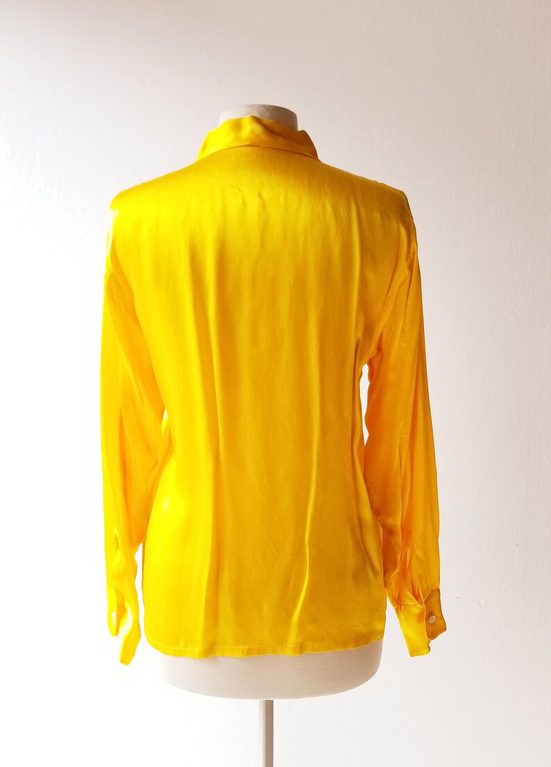 Puede incluir: Una blusa de sat&eacute;n amarillo brillante con mangas largas y cuello abotonado.