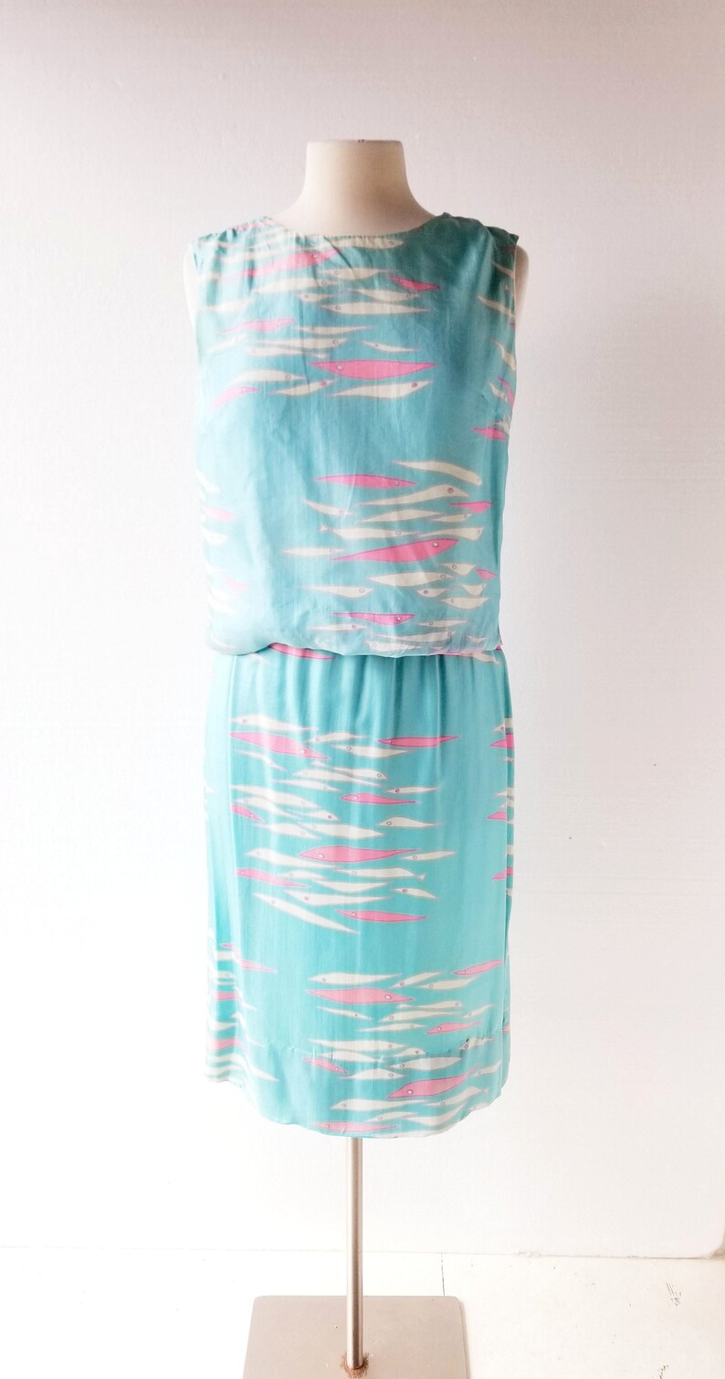 May include: A sleeveless dress with a blue background and a white and pink fish pattern. The dress has a fitted bodice and a flowing skirt.