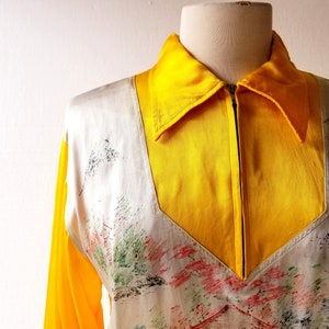 Puede incluir: Una camisa de manga larga amarilla y blanca con cierre de cremallera y un panel blanco con un dise&ntilde;o pintado a mano de una pagoda japonesa y &aacute;rboles.