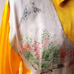 Puede incluir: Una camisa blanca con cuello amarillo y mangas largas. La camisa tiene un dise&ntilde;o de inspiraci&oacute;n japonesa con una monta&ntilde;a, &aacute;rboles y una pagoda impresos en la parte delantera.