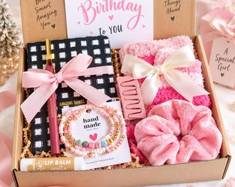 May include: A birthday gift box containing a black and white checkered notebook with a pink ribbon, a pink pen, a vanilla lip balm, a beaded bracelet with the word LOVE, a pink hair claw clip, a pink scrunchie, and a pair of pink fuzzy socks.