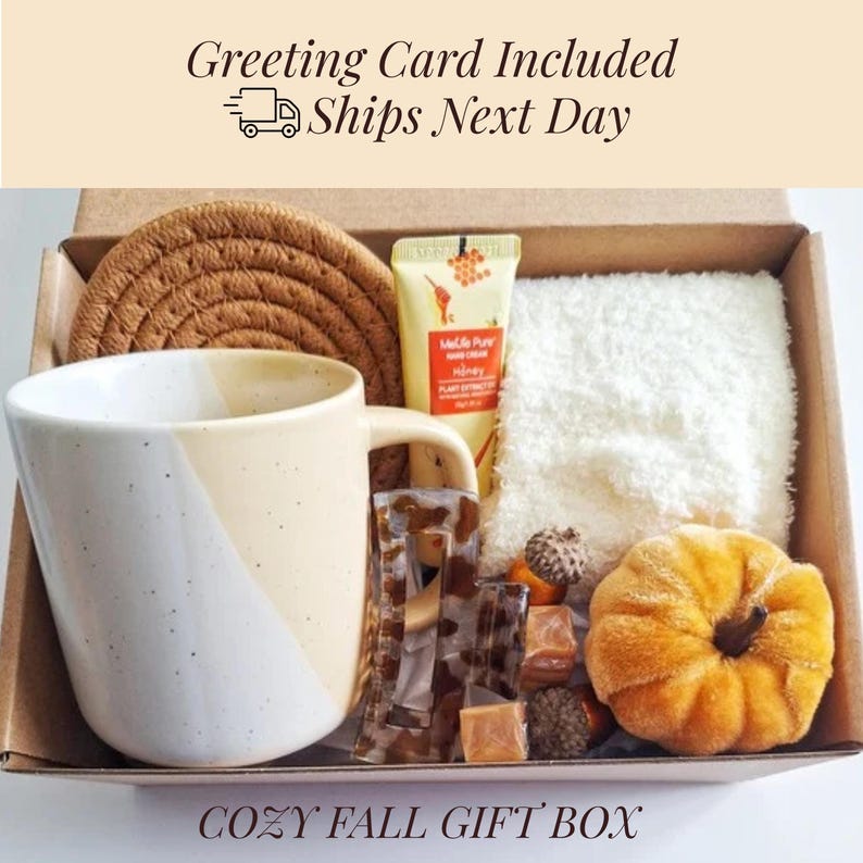 May include: A cozy fall gift box filled with a mug, hand cream, a coaster, a small towel, a decorative pumpkin, and candies. The mug is white and beige. The box includes the text "Greeting Card Included Ships Next Day" and "COZY FALL GIFT BOX".