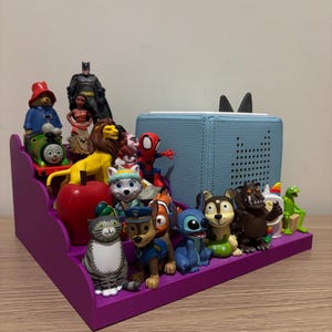 May include: A purple tiered shelf displaying various figurines, including a bear, Thomas the Tank Engine, Batman, a lion, Spider-Man, and characters from Paw Patrol and Disney movies. A light blue speaker is also present.