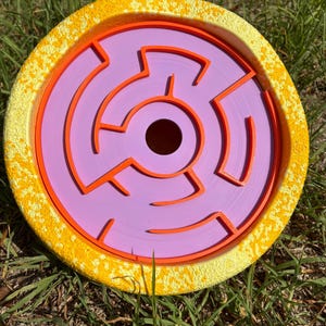 May include: A yellow and orange dog puzzle toy with a purple maze in the centre. The maze has a hole in the centre for treats.