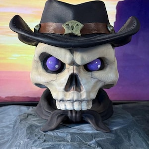 May include: A skull wearing a black cowboy hat with a brown leather band and a metal star-shaped badge. The skull has purple eyes and a black bandana around its neck. The background is a purple and orange sunset.