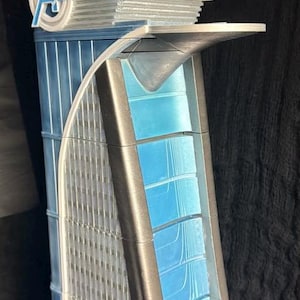 Op de afbeelding: Een gedetailleerd model van de Avengers Tower, een fictieve wolkenkrabber uit het Marvel Cinematic Universe. Het model is gemaakt van grijs en blauw plastic en heeft het Avengers-logo aan de voorkant.