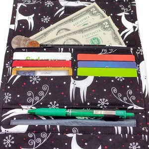 May include: Black and white patterned wallet with a reindeer and snowflake design. The wallet is open, revealing cash, coins, credit cards, and a green pen. The wallet is made of fabric.