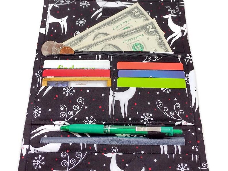 May include: Black and white patterned wallet with a reindeer and snowflake design. The wallet is open, revealing cash, coins, credit cards, and a green pen. The wallet is made of fabric.