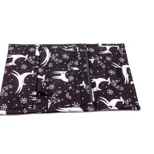 May include: Black and white fabric wallet with a zipper closure. The wallet features a repeating pattern of white deer, snowflakes, and swirls on a black background. The wallet is open, revealing multiple compartments.