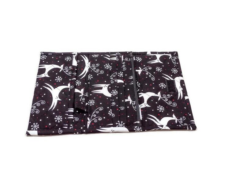 May include: Black and white fabric wallet with a zipper closure. The wallet features a repeating pattern of white deer, snowflakes, and swirls on a black background. The wallet is open, revealing multiple compartments.