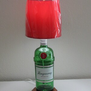 May include: A red lampshade with a green glass bottle base. The bottle is labeled "Tanqueray Imported London Dry Gin".
