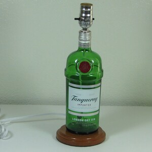 May include: A green glass bottle lamp with a wooden base. The bottle is labeled "Tanqueray Imported London Dry Gin".
