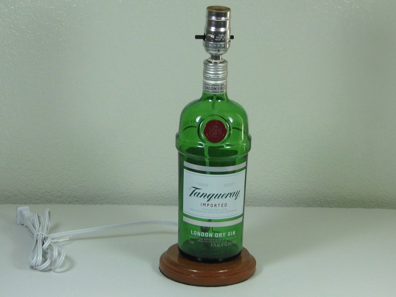 May include: A green glass bottle lamp with a wooden base. The bottle is labeled "Tanqueray Imported London Dry Gin".