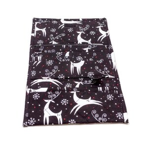 May include: Black fabric wallet with a white reindeer and snowflake pattern. The wallet has multiple compartments and a zipper closure. The design includes red accents and a quilted texture, suggesting a holiday theme.