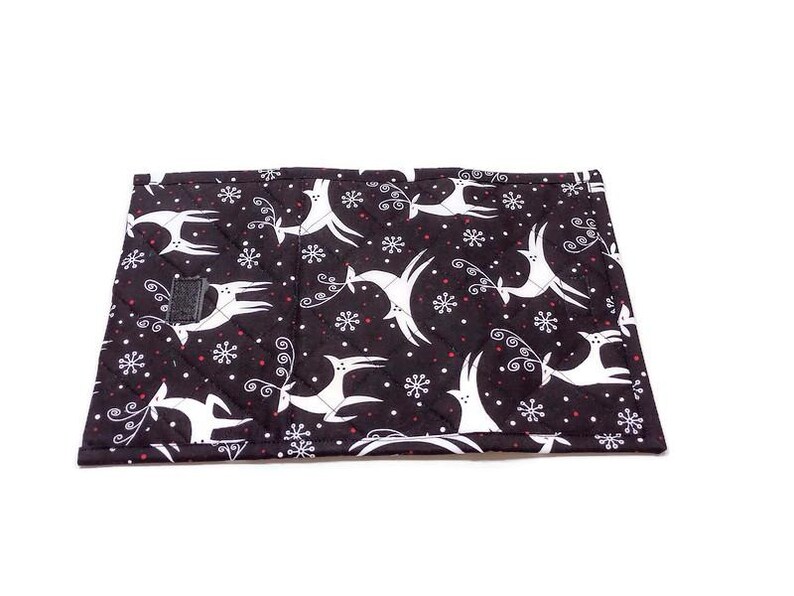 May include: A black quilted fabric item with a white reindeer and snowflake pattern. The reindeer are leaping, and the snowflakes are small and white. The item has a small black velcro closure.