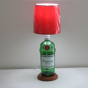 May include: A red lampshade with a green glass bottle base. The bottle is labeled "Tanqueray Imported London Dry Gin".