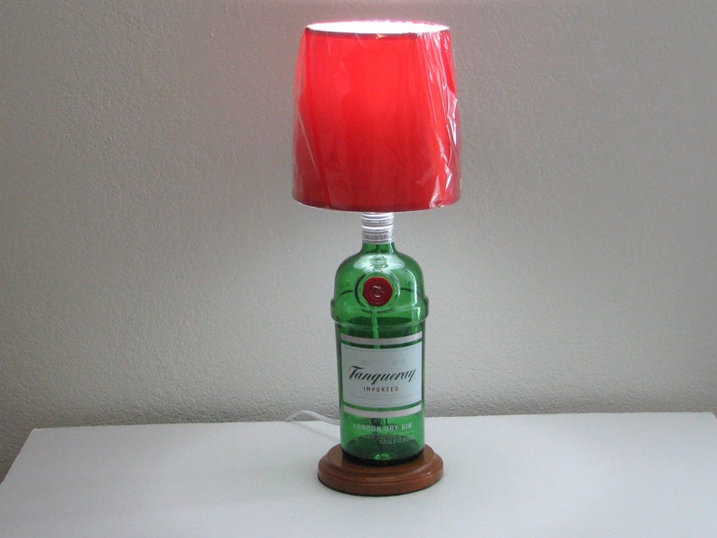 May include: A red lampshade with a green glass bottle base. The bottle is labeled "Tanqueray Imported London Dry Gin".