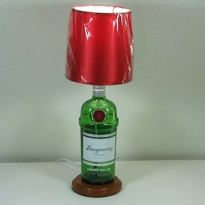 May include: A table lamp made from a green glass Tanqueray London Dry Gin bottle with a red fabric lampshade.