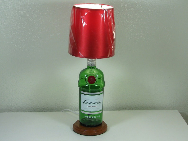 May include: A table lamp made from a green glass Tanqueray London Dry Gin bottle with a red fabric lampshade.
