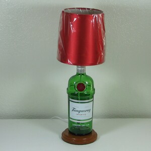 May include: A table lamp made from a green glass bottle with a red fabric lampshade. The bottle is labeled "Tanqueray Imported London Dry Gin".