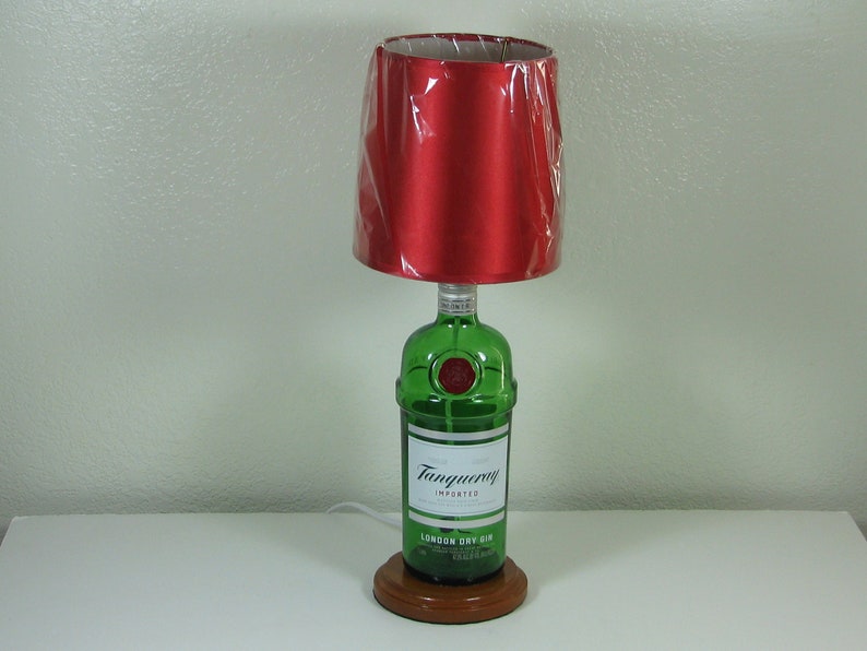 May include: A table lamp made from a green glass bottle with a red fabric lampshade. The bottle is labeled "Tanqueray Imported London Dry Gin".