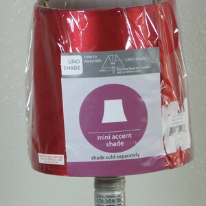 May include: Red lampshade with a white label that says "UNO SHADE" and instructions on how to assemble the shade. The label also includes a diagram of a lampshade and the text "mini accent shade" and "shade sold separately".