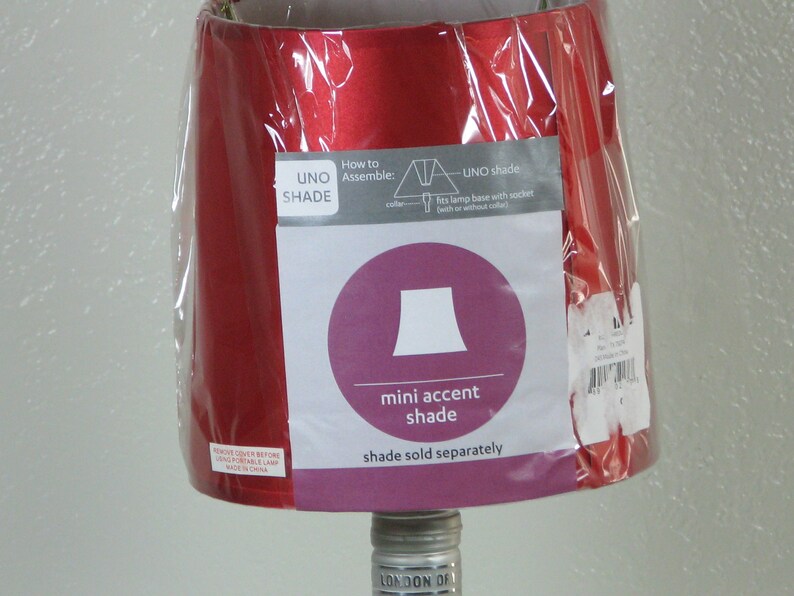 May include: Red lampshade with a white label that says "UNO SHADE" and instructions on how to assemble the shade. The label also includes a diagram of a lampshade and the text "mini accent shade" and "shade sold separately".