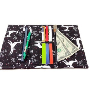 May include: Black fabric wallet with a white deer and snowflake pattern. The wallet is open, revealing pens, credit cards, and a dollar bill. The wallet is designed to hold various items.