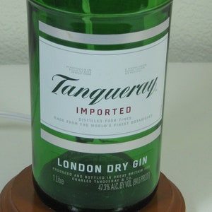 May include: A green glass bottle of Tanqueray London Dry Gin. The label is white with black text and says "IMPORTED, DISTILLED FOUR TIMES, MADE FROM THE WORLD'S FINEST BOTANICALS, LONDON DRY GIN, PRODUCED AND BOTTLED IN GREAT BRITAIN FOR CHARLES TANQUERAY & CO., 1 Litre, 47.3% ALC. BY VOL. 194 & PROOF".