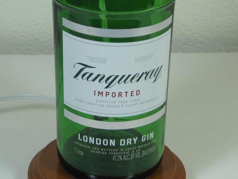 May include: A green glass bottle of Tanqueray London Dry Gin. The label is white with black text and says "IMPORTED, DISTILLED FOUR TIMES, MADE FROM THE WORLD'S FINEST BOTANICALS, LONDON DRY GIN, PRODUCED AND BOTTLED IN GREAT BRITAIN FOR CHARLES TANQUERAY & CO., 1 Litre, 47.3% ALC. BY VOL. 194 & PROOF".