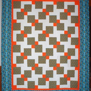 May include: A quilt with a white background and a pattern of orange and green squares. The quilt is bordered with a blue and white fabric.