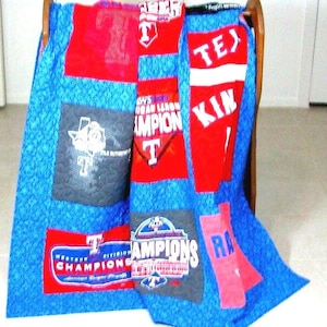 May include: A blue and red patchwork quilt made from repurposed t-shirts. The quilt features the words "Texas", "Champion", "Western Division Champions", and "Kin".