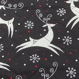 May include: Black quilted fabric with a repeating pattern of white reindeer and snowflakes, accented with small red dots. The reindeer have stylized antlers and are in various poses. A festive, winter-themed design.
