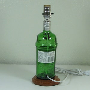 May include: A green glass bottle lamp with a wooden base and a white cord. The bottle has a label with the text "Bombay Sapphire" on it.