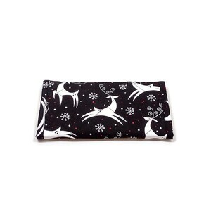 May include: A folded black fabric item with a white reindeer and snowflake pattern. The reindeer are stylized with curved lines, and the snowflakes have six points. Small red dots are scattered throughout the design.