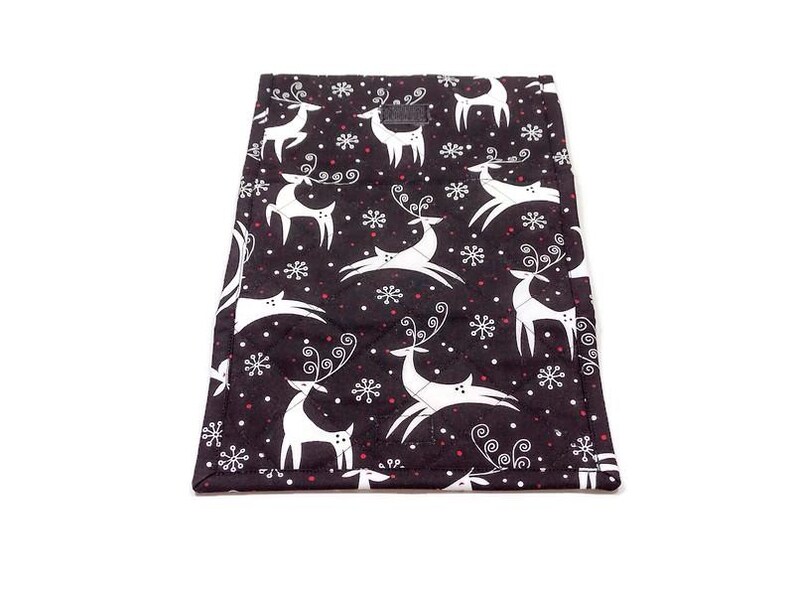 May include: Black quilted fabric with a white reindeer and snowflake pattern. The reindeer have large antlers and are in various poses. Red dots are interspersed among the snowflakes. The edges are finished with a white border.