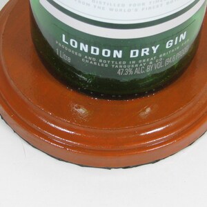 May include: A green glass bottle of London Dry Gin, with a label that reads "London Dry Gin" and "1 Litre". The bottle is sitting on a round, orange coaster.