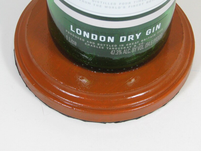 May include: A green glass bottle of London Dry Gin, with a label that reads "London Dry Gin" and "1 Litre". The bottle is sitting on a round, orange coaster.