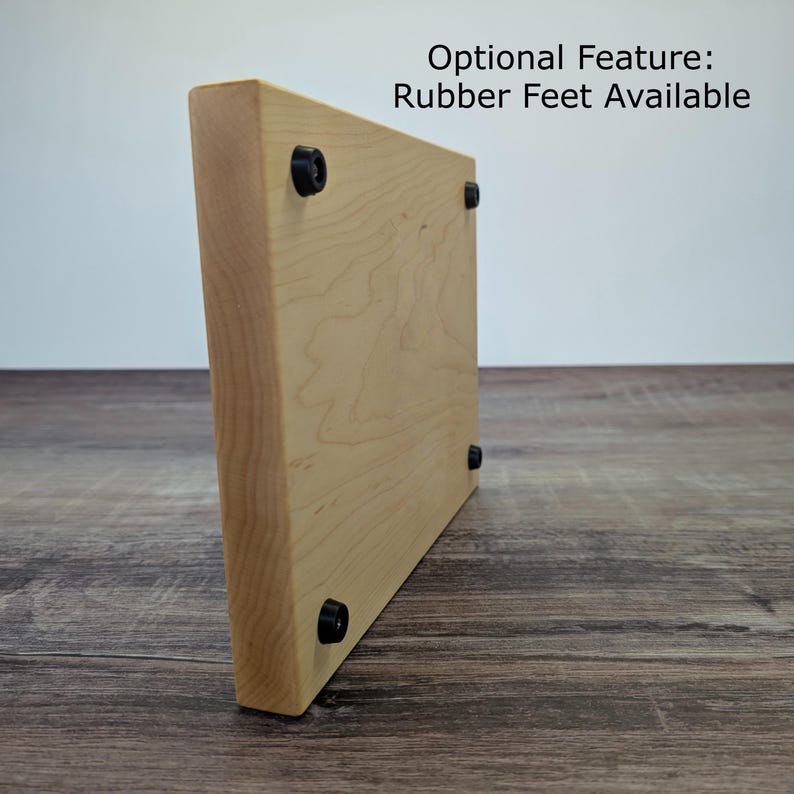 Op de afbeelding: Een lichtgekleurde houten snijplank met afgeronde hoeken. De plank heeft zwarte rubberen voetjes aan de onderkant. De tekst "Optional Feature: Rubber Feet Available" is zichtbaar. De houtnerf is zichtbaar.