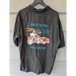 May include: Black button-up shirt with a Harley-Davidson motorcycle graphic on the back. The graphic features a red motorcycle with the text "KING OF THE ROAD" and "HARLEY-DAVIDSON" in blue.