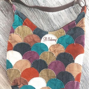 Peut inclure: Un sac à bandoulière en velours côtelé marron avec une bandoulière en cuir marron. Le sac est décoré d'un patchwork de formes écaillées colorées. Le sac porte un logo Billabong brodé sur le devant.