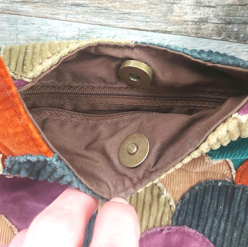May include: A patchwork purse made of corduroy fabric in various colors, including brown, green, purple, and orange. The purse has a zipper closure and two magnetic closures.