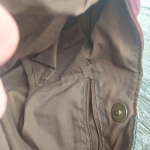 May include: The inside of a brown fabric bag with a zippered pocket and a snap closure. The bag has a brown lining and a zippered pocket.