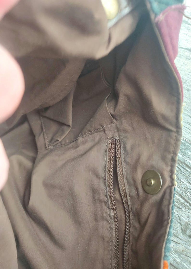 May include: The inside of a brown fabric bag with a zippered pocket and a snap closure. The bag has a brown lining and a zippered pocket.