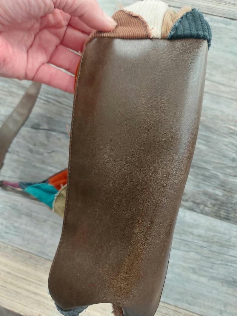 May include: A brown leather bag with a patchwork design of corduroy fabric in various colors, including beige, brown, and green.