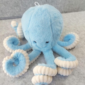 May include: A plush blue octopus toy with white accents on its tentacles. The stuffed animal has a round head and eight arms. The toy has a loop at the top for hanging.