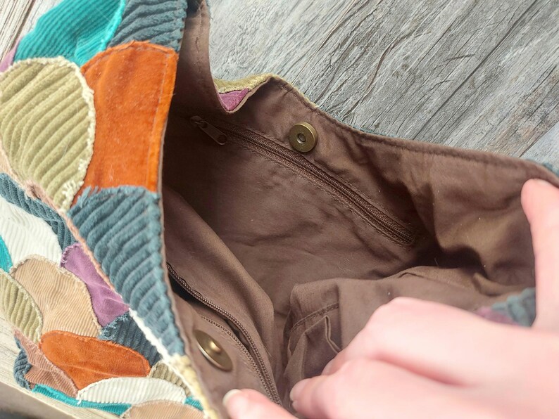 May include: A patchwork tote bag with a brown fabric lining. The bag is made of different colored corduroy fabrics, including green, orange, and brown. The bag has a zippered pocket on the inside.